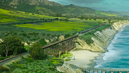 A historic trestle bridge arcs along rugged coastal cliffs where emerald farmland meets the Pacific shore.