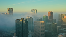 Morning fog rolls through downtown skyscrapers as golden sunrise light breaks across the skyline.