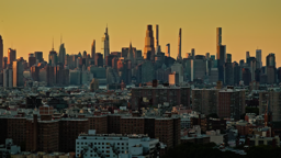Manhattan's glittering skyline rises beyond Brooklyn's rooftops in the warm glow of dusk.